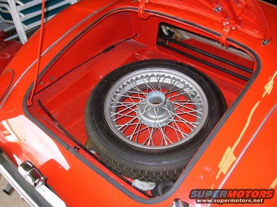 Red car trunk interior with a wire-spoke spare tire and a Supermotors.net watermark