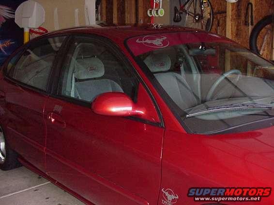 Red sedan parked in garage, showing side and front quarter view. Interior has cloth seats with headrests