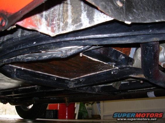 Underside view of a car's frame and floor pan, showing some rust and repairs