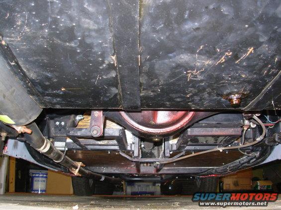 Underside view of a car's rear axle, exhaust, and fuel tank. Shows suspension components and underbody