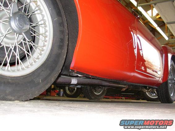 Low angle shot of a red sports car's side and undercarriage, showing wire wheels and exhaust