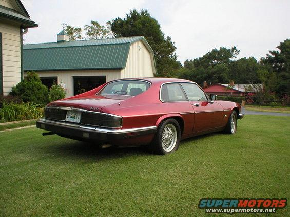 Red 1992 Jaguar XJ-S coupe parked on a lawn in front of a house and barn