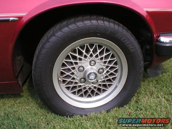 Red Jaguar XJ-S wheel with a mesh alloy rim and a Jaguar emblem, seen from the side