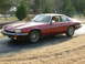 1992 Jaguar XJ-S - A maroon Jaguar XJ-S coupe sits on a driveway during a cloudy day, with dry grass and trees in the background.