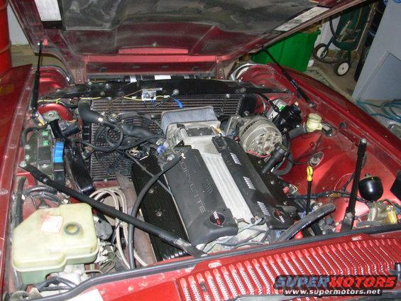 Red car engine bay with a Corvette engine. Visible text includes "CORVETTE"