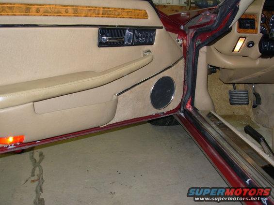 Close-up of a car's interior door panel, speaker, and part of the dashboard with pedals visible