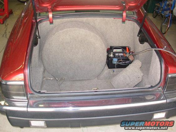 Red Jaguar XJ-S trunk interior with spare tire well and battery
