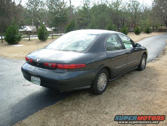 Dark sedan parked on a paved driveway, rear-left quarter view. The car has a license plate reading '754-FJY'