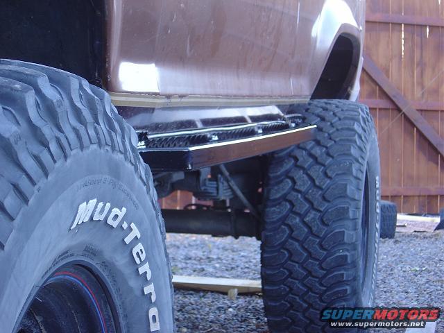 Side view of a brown SUV with large off-road tires and a step bar