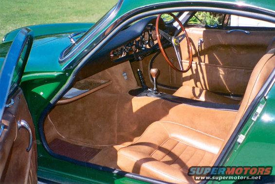 Interior view of a green vintage sports car with tan leather seats and wooden steering wheel