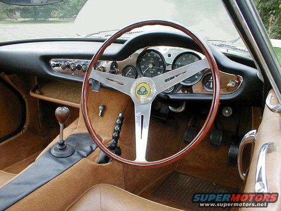 Car interior with wood-rimmed steering wheel, Lotus badge, and dashboard gauges