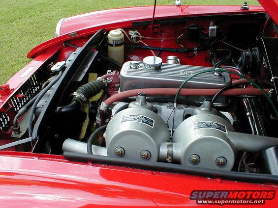 Red car engine bay with dual SU carburetors and an MG branded valve cover