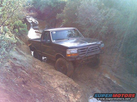 Black Ford F-150 off-roading on a muddy trail with lifted suspension and off-road tires