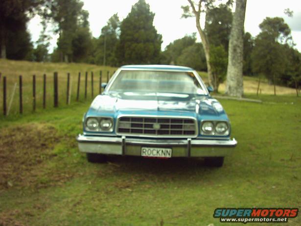 Blue sedan parked on grass with a fence behind it