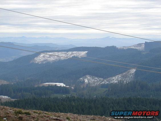 Overhead power lines cross a vast mountain landscape with patches of snow on the hillsides