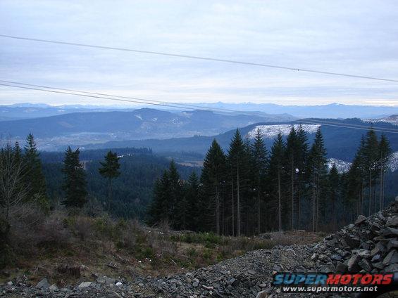 Mountain view with trees and power lines overhead. Some snow on distant peaks
