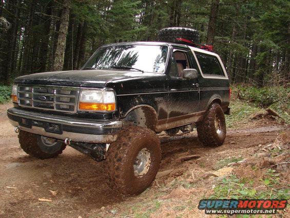 Black 1996 Ford Bronco with large off-road tires on a muddy forest trail