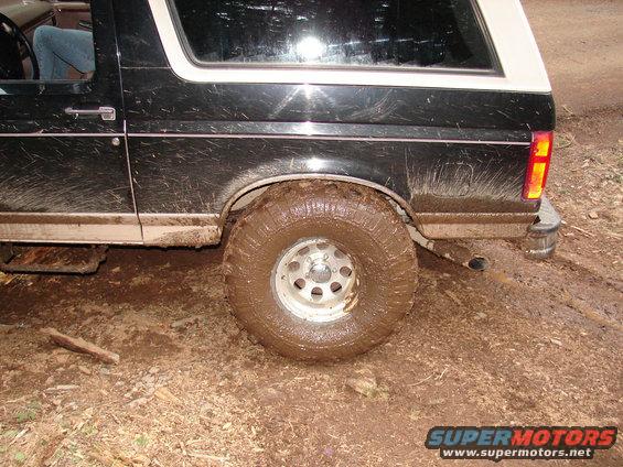 Muddy 1996 Ford Bronco rear side view, showing the tire, fender, and part of the door