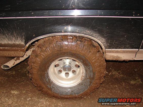 Mud-covered tire and fender of a dark-colored vehicle, with exhaust pipe visible