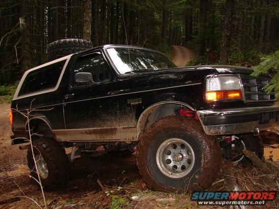 Black 1996 Ford Bronco with lifted suspension navigating a muddy forest trail