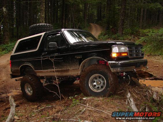 Black 1996 Ford Bronco driving on a muddy trail in a forest