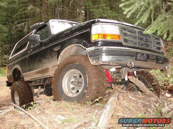 Black 1996 Ford Bronco with large tires stuck in mud on a wooded trail