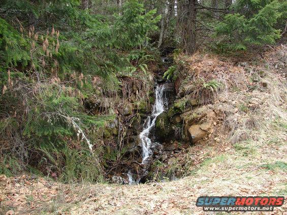 Waterfall cascading down a rocky, wooded hillside with dry grass and pine trees