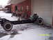 1960 Ford Falcon - A vehicle chassis with an engine is parked outside a garage in snowy conditions.