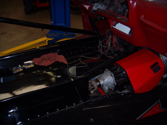 Interior of a vehicle with exposed wiring and a red housing unit near the transmission tunnel