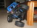 1990 Ford Bronco - A black remote control toy truck with a blue roll cage is tilted on a carpeted floor next to a wooden table.
