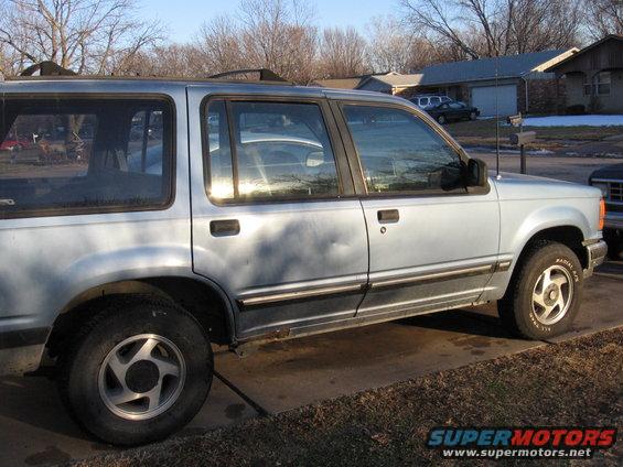 Light blue SUV side view, dent on driver's door, chrome trim, aftermarket wheels