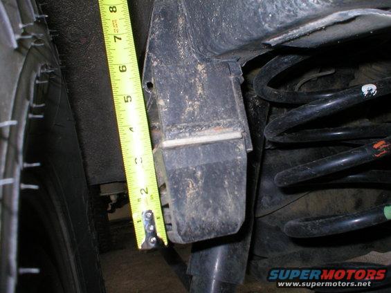Tape measure next to a vehicle's rear coil spring and suspension component