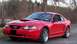 2004 Ford Mustang - A red 2004 Ford Mustang coupe is parked outdoors with a hood scoop and chrome wheels.