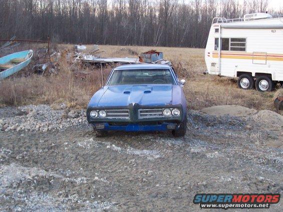 Front view of a blue 1968 Pontiac Firebird with hood scoops parked on gravel