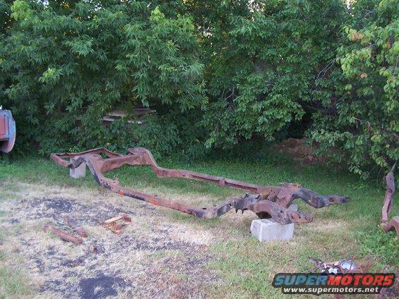 rusted vehicle frame sitting on grass, supported by concrete blocks