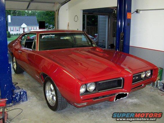 Red 1969 Pontiac GTO in garage on lift. Has 'YearOne' sticker on windshield