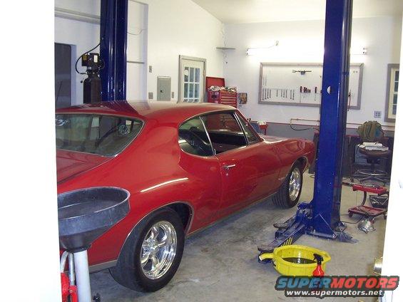 Red 1967 coupe on a car lift in a garage, with a drain pan and tools visible