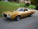 1972 Ford Ranchero - This gold pickup truck with an orange stripe is seen from a 3/4 front angle. Another vehicle is visible in the background on a grassy hill.