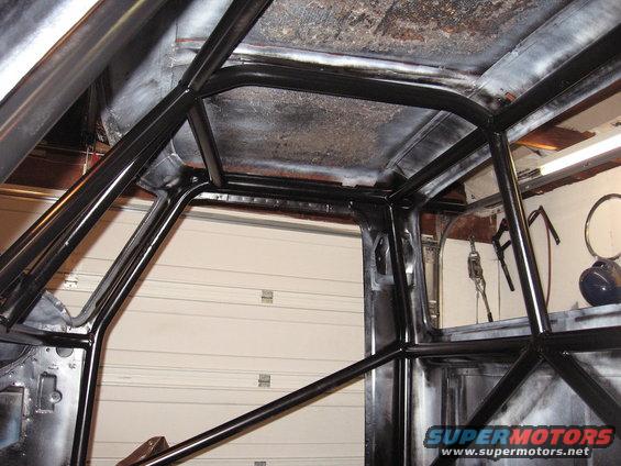 Interior of a vehicle with a black roll cage installed. The ceiling and walls appear to be prepped for paint
