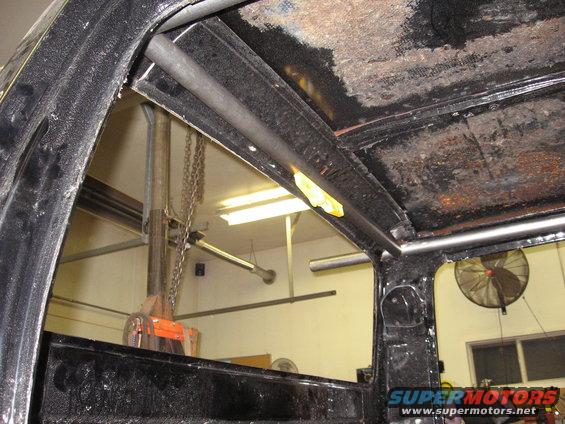 Interior view of a truck cab, showing a roll cage installed above the driver and passenger area. The ceiling is rough and shows signs of rust