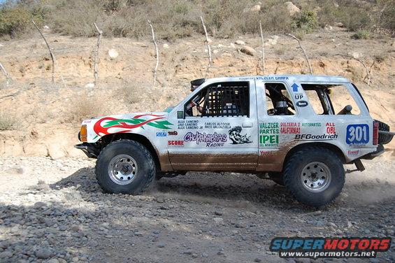 White off-road SUV with racing decals and number 301, seen from the side on a dirt road