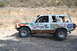 1992 Ford Explorer - A white off-road SUV with racing decals drives on a dirt road, kicking up dust.