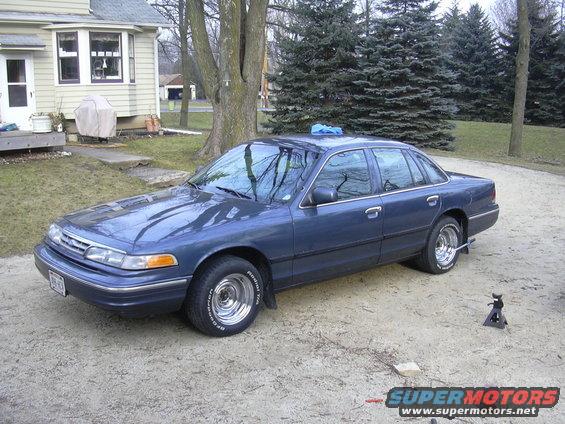 Blue Ford Crown Victoria parked in a driveway with a house in the background