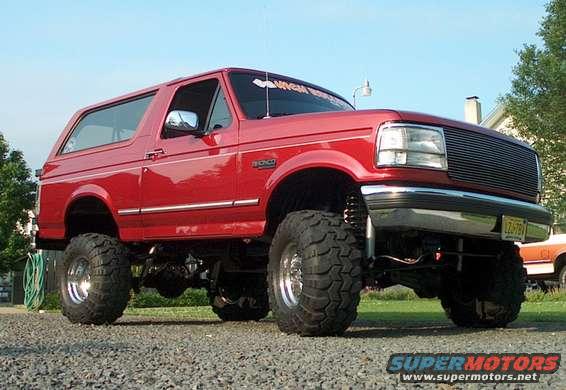 Red 1994 Ford Bronco with lifted suspension and large off-road tires parked on a gravel surface