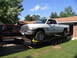 1995 Ford C-350 (Centurion Conversions) - A white Dodge Ram pickup truck is loaded onto a trailer in front of a brick house.