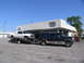 1995 Ford C-350 (Centurion Conversions) - A dark green SUV tows a white pickup truck on a trailer in front of Dorsey Trailer Sales.