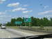 1995 Ford C-350 (Centurion Conversions) - A silver minivan travels on a highway under a blue sky with scattered clouds, passing welcome signs.