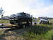 1995 Ford C-350 (Centurion Conversions) - A dark blue Ford Bronco is being transported on a trailer, with a white pickup truck visible in the background.