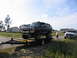 1995 Ford C-350 (Centurion Conversions) - A dark blue Ford Bronco is loaded onto a trailer, with a white pickup truck visible in the background.