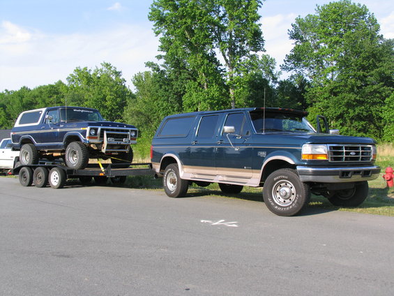 Dark blue Ford Bronco on a trailer, towed by a dark green Ford F-Series SUV